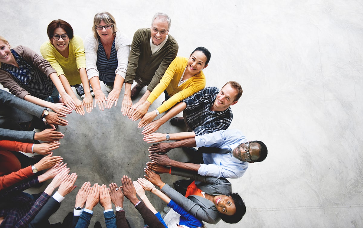 Above view of a group of people standing in a circle holding their arms out to form a circle with their hands