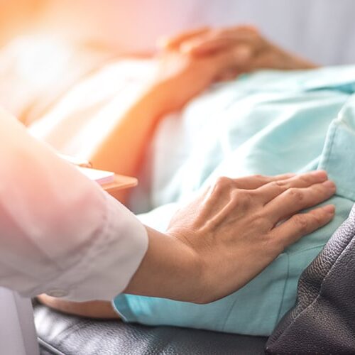 Elderly woman laying in hospital bed while practitioner consoles her by putting their hand on her shoulder